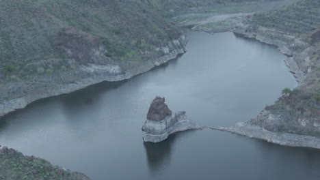 Sorrueda-dam,-Gran-Canaria:-aerial-view-over-the-famous-dam-and-flying-over-one-of-the-rock-formations-and-with-completely-calm-water