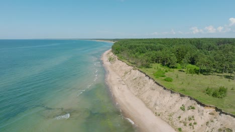 Aerial-establishing-view-of-Baltic-sea-beach-at-Jurkalne-on-a-sunny-summer-day,-white-sand-cliff-damaged-by-waves,-coastal-erosion,-climate-changes,-wide-drone-shot-moving-forward
