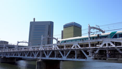 TOKYO,-JAPAN---APRIL-9,-2023:-Tokyo-train-near-Sumida-river-walk,-view-from-Asakusa-district-in-Tokyo,-Japan