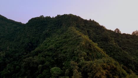 Cinematic-drone-shot-of-overgrown-mountains-lighting-by-sun-in-the-morning---Asia,-Indonesia