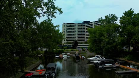 Un-Dron-4k60-Se-Revela-Detrás-De-árboles-Con-Vista-A-Recorridos-En-Bote-Público-Para-La-Comunidad-De-Laval,-Costa-Sur-De-Quebec,-Con-Botes-De-Alquiler,-Recorridos-En-Kayak-Y-Nadie-Afuera-En-Aguas-Planas-Parcialmente-Nubladas