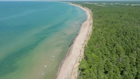 Aerial-establishing-view-of-Baltic-sea-beach-at-Jurkalne-on-a-sunny-summer-day,-white-sand-cliff-damaged-by-waves,-coastal-erosion,-climate-changes,-wide-drone-shot-moving-forward,-tilt-down