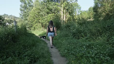Woman-and-her-dog-taking-a-walk-along-a-narrow-path-in-the-countryside