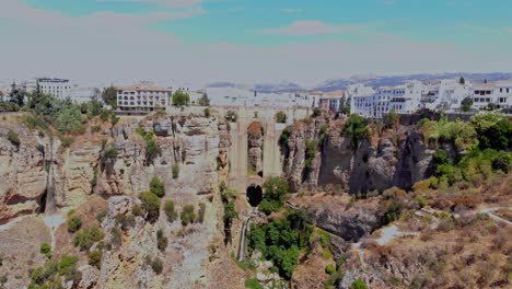 Drone-footage-backing-out-far-and-high,-filming-the-bridge-by-the-high-cliff-gap-in-Ronda,-Spain