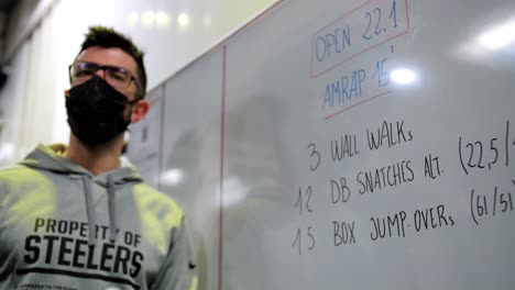 CrossFit-Coach-Presents-Competition's-WOD-of-the-Day,-Demonstrating-Step-by-Step-on-Whiteboard