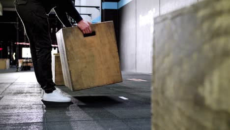 Man-Placing-Jump-Box-for-CrossFit-Competition-in-the-Center-of-Rubber-Floor-Gym,-Illuminated-by-Background-Lighting