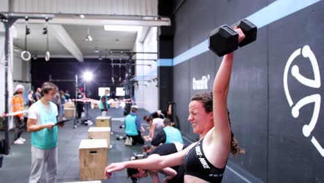 Valor-Y-Fuerza:-Chica-Morena-Con-Coletas-Empujando-Fragmentos-En-Una-Competencia-De-Crossfit,-El-Fondo-Presenta-A-Otros-Competidores