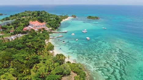 Aerial-orbiting-shot-of-luxury-hotel-resort-in-Cayo-Levantado-island-during-sunny-day-with-parking-boats-and-coral-reef-in-clear-Caribbean-sea-water---Samana,-Dominican-Republic