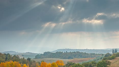 Autumn-landscape-in-Tuscany,-farms,-trees-and-hills,-cloudy-sky,-Sunbeams-Piercing-Cloud-Cover---4k-time-lapse-footage