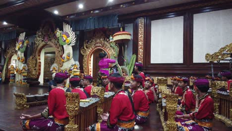 Balinese-Priestess-Blesses-Musicians-at-Gamelan-Music-Performance-Bali-Indonesia-with-Holy-Water-around-Flower-Arrangements