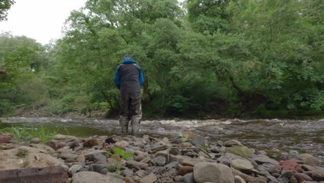 Static-shot-of-a-fisherman-wading-and-fly-fishing-a-small-fast-river