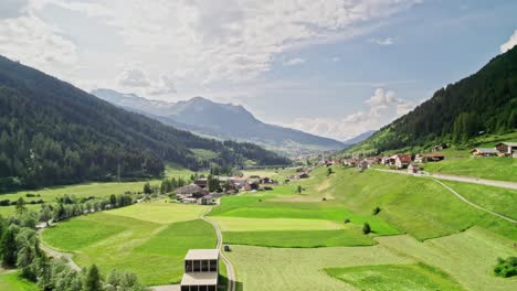 Drone-flight-over-green-pastures-towards-the-town-of-Cadras-in-Switzerland