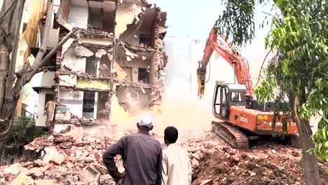 Hombres-Indios-Mirando-Excavadora-Con-Martillo-Demoliendo-Un-Pequeño-Edificio.