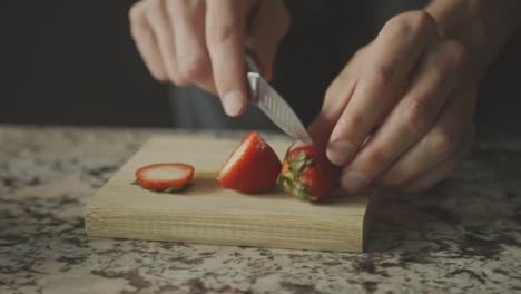 Slicing-Two-Fresh-Strawberries-On-A-Wooden-Board