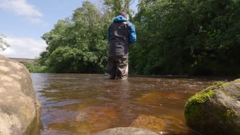Low-angle-shot-of-a-fisherman-wading-and-fly-fishing-in-murky-brown-water
