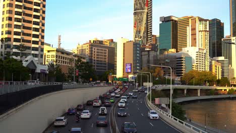 Dynamic-zoom-in-shot-capturing-rush-hour-inbound-and-outbound-vehicle-traffics-on-M3-Pacific-Motorway-with-riverside-downtown-cityscape-in-the-background-at-sunset-golden-hours