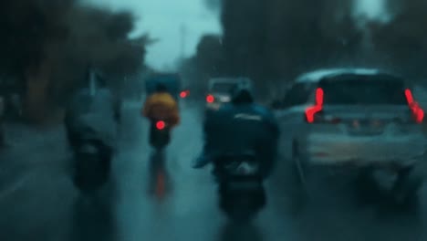 Blurred-night-shot-on-the-mirror-while-raining-and-movement-camera,-Focused-car-cabin-selection-background,-bike-driving-on-a-opposite-lane-through-a-car-front-wet-window-with-raindrops
