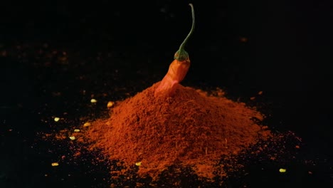 Slow-motion-spicy-whole-red-chilli-pepper-falling-into-pile-of-savoury-paprika-powder-isolated-on-black-background-studio-shot