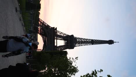 Toma-Vertical-De-Lugareños,-Turistas-Y-La-Torre-Eiffel-En-París,-Francia-Al-Atardecer.