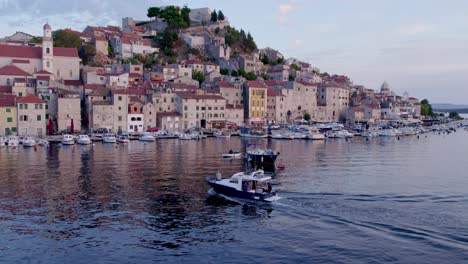 Drone-view-of-Sibenik-town-in-Croatia-during-sunset-with-motorboat,-aerial