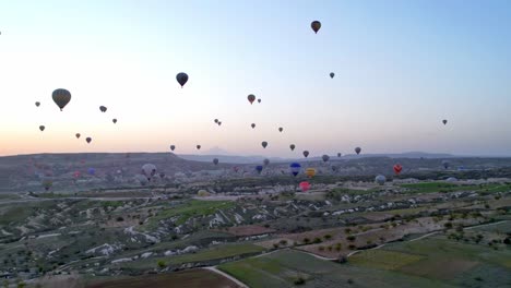 Aerial-drone-camera-follows-Goreme-town-on-sunset-in-Cappadocia,-Central-Anatolia,Turkey,-Colorful-hot-air-balloons-before-launch-at-Cappadocia,-Turkey