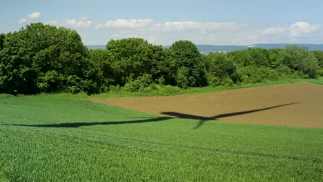 Shadows-of-a-spinning-wind-turbine-in-beautiful-summer-panorama-scenery,-meadow