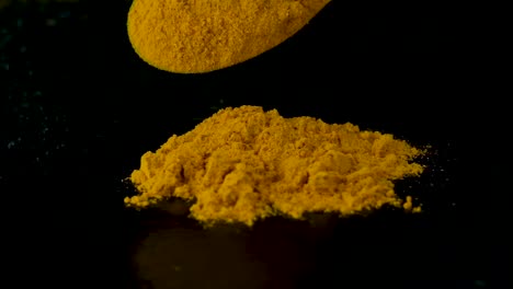 Slow-motion-spicy-yellow-aromatic-turmeric-falling-from-wooden-spoon-onto-pile-isolated-on-black-background,-Studio-shot