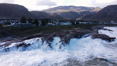 Strong-waves-crash-into-rocky-coastline-of-Hermanus,-mountain-background