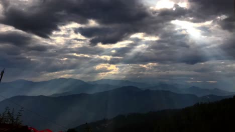 Windstorm,-Timelapse-of-sun-rays-emerging-though-the-dark-storm-clouds-in-the-mountains,-Dramatic-clouds,-forest-area,-and-the-trees