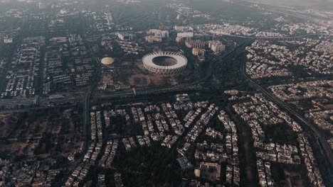 Aerial-shot-of-Surat-city,-a-community-in-Surat,-India,-large-cricket-stadium-is-visible-when-aerial-camera-is-moving-forwards,-Beautiful-clouds-sky-on-city-view-from-aeroplane-window
