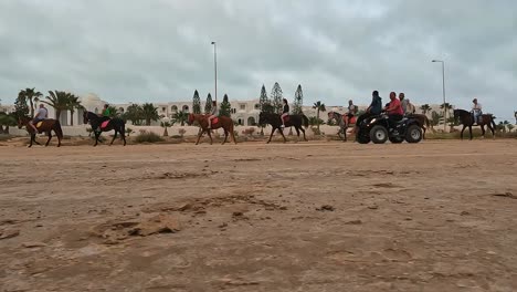 Punto-De-Vista-De-La-Superficie-Del-Suelo-En-ángulo-Bajo-De-Una-Caravana-De-Carruajes-De-Caballos-Y-Camellos-A-Través-Del-Desierto-De-Djerba,-Túnez