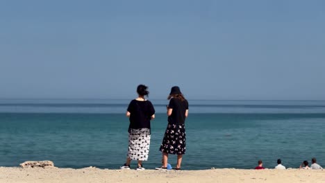 Happy-female-tourist-walks-barefoot-on-a-sandy-beach-in-the-JBR-area-of-Dubai,-Beautiful-woman-walking-on-the-beach-in-Dubai