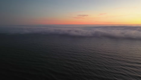 Aerial-view-tilting-over-the-sea,-revealing-a-wall-of-coastal-fog,-Haar-or-Seafret,-during-dusk