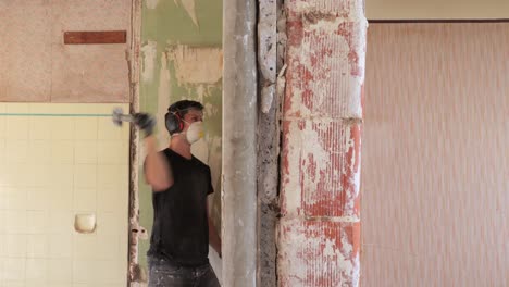 Young-male-amateur-contractor-demolishing-a-wall-with-a-short-sledge-hammer
