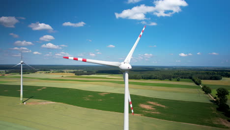 Aerial-wide-shot-of-rotating-wind-turbine-on-agricultural-grass-field-during-sunny-day---Establishing-drone-shot---trucking-shot