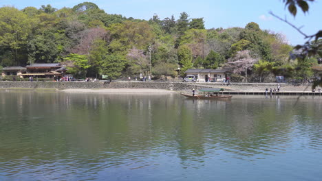 KYOTO,-JAPAN---April-4,-2023:-Tourists-rowing-boat-in-Katsura-River-in-Arashiyama-district-with-cherry-blossom-in-spring-time