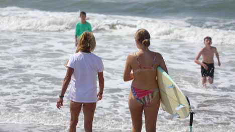 Zwei-Frauen-Gehen-Mit-Einem-Surfbrett-In-Die-Brandung-Am-Strand