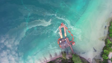 Aerial-birdseye-flying-over-pier-in-Pragser-Wildsee,-clear-emerald-waters,-Italy