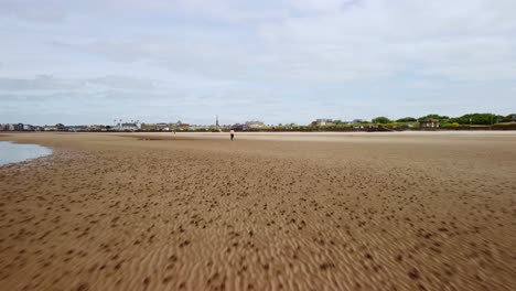 An-adult-male-running-in-the-distance-on-a-beach-with-sand-and-water