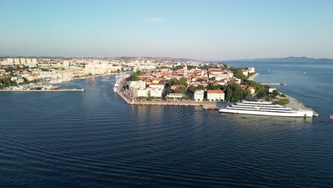 Beautiful-colours-an-aerial-view-over-Zadar-city-with-old-town-peninsula,-luxury-cruise-ship-docked-and-few-smaller-ones-sailing-to-marina