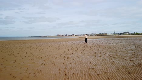 Aerial-dolly-footage-of-a-young-man-on-a-beach-near-the-water’s-edge