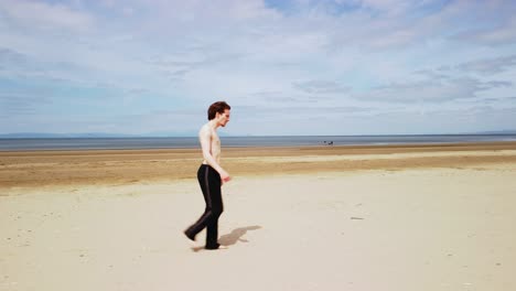 Side-tracking-shot-of-young-shirtless-man-walking-on-a-sandy-beach