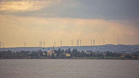 Wind-turbines-generate-clean-energy-with-Larnaca-Salt-Lake,-Cyprus-in-the-foreground---time-lapse