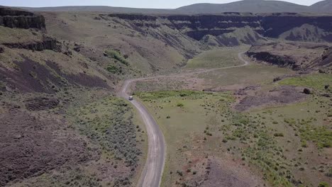 Aerial-tracks-white-van-driving-dirt-road-into-stunning-Moses-Coulee