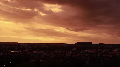 Dramatischer-Sonnenuntergang-Am-Orangefarbenen-Himmel-Mit-Hintergrundbeleuchtung-Der-Stadt-Vom-Berggipfel-Am-Abend.-Das-Zeitraffervideo-Wurde-In-Jodhpur,-Rajasthan,-Indien,-Aufgenommen