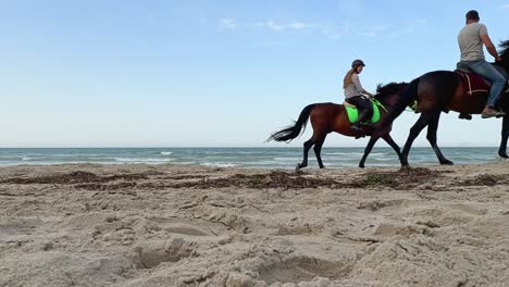 Low-angle-view-of-two-tourists-riding-horses-at-on-sandy-beach
