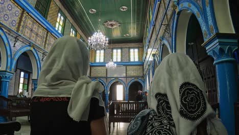 Rückansicht-Von-Zwei-Touristischen-Frauen-Mit-Kopftuch,-Die-In-Der-Jüdischen-Synagoge-El-Ghriba-Von-Djerba-In-Tunesien-Sitzen