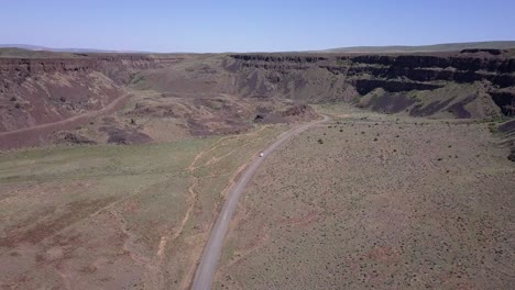 Aerial:-Lone-vehicle-drives-lonely-road-through-scablands-canyon,-WA