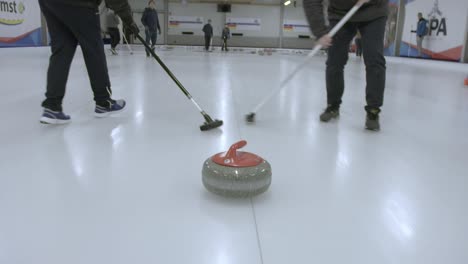 Siguiente-Piedra-De-Curling-Con-Dos-Jugadores-Barriendo-Delante-De-Ella