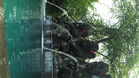 Toma-Vertical-En-Cámara-Lenta-De-Una-Hermosa-Piscina-En-Bali,-Indonesia,-Con-Esculturas-De-Las-Que-Fluye-El-Agua-Durante-Un-Viaje-De-Vacaciones-A-Través-De-Ubud